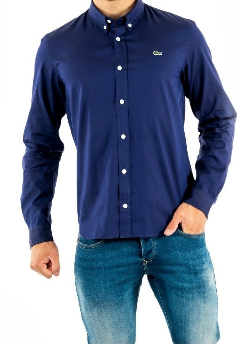 Mörkblå knapp-up skjorta i bomull med krage, med vita knappar och en liten grön logotyp på bröstet. Bärs med blå jeans.