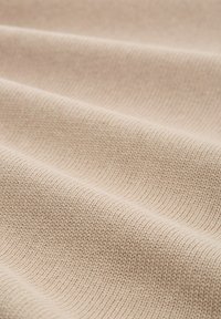 Meki bež pleteni materijal s vidljivom rebrastom teksturom i blagim naborima koji stvaraju valoviti uzorak po površini.