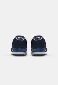 Ténis de corrida na cor azul-marinho com parte superior em camurça e malha, detalhes em cinza e sola em borracha. Apresenta "1973" em relevo e o nome da marca no calcanhar.