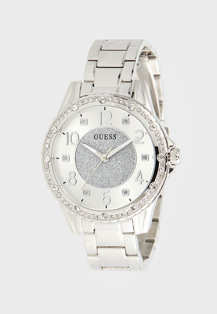 Orologio in acciaio inox argento con quadrante luccicante, bezel con cristalli, numeri grandi e uno stile di bracciale elegante. Nome del marchio "GUESS" in evidenza.