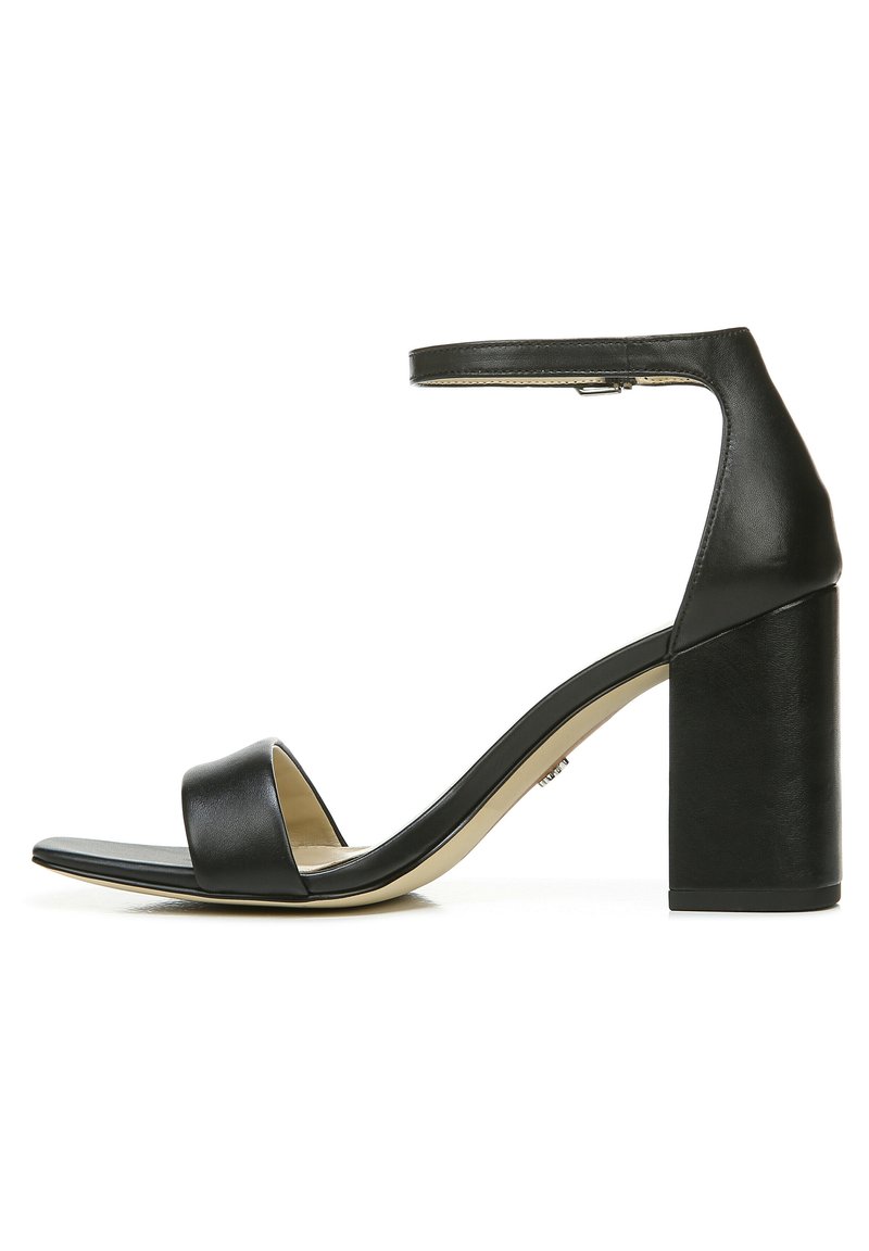 Zwarte leren hak sandaal met een brede teband en enkelband. Blokkenhak en een zachte textuur, met een beige binnenzool voor contrast.