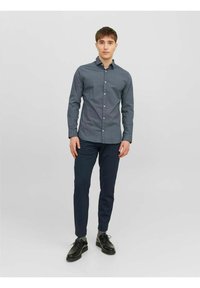 Camicia button-up in navy con un piccolo motivo a quadretti, abbinata a pantaloni scuri e scarpe nere. Vestibilità moderna, texture liscia e maniche lunghe.