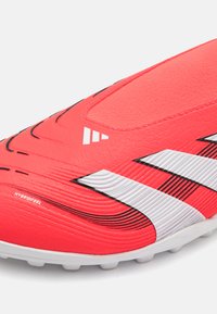 Red soccer cleat with a textured synthetic upper, featuring black accents and three white stripes. Closed design with a smooth finish.