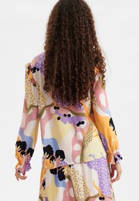 Kleurige blouse met lange mouwen, gekenmerkt door een mix van abstracte patronen in geel, roze, blauw en zwart, met ruches aan de mouwen.