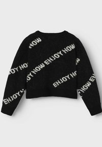 Svart kort tröja med en fluffig textur, med vit text "ENJOY NOW" diagonalt över kroppen och ärmarna. Rund halsringning.