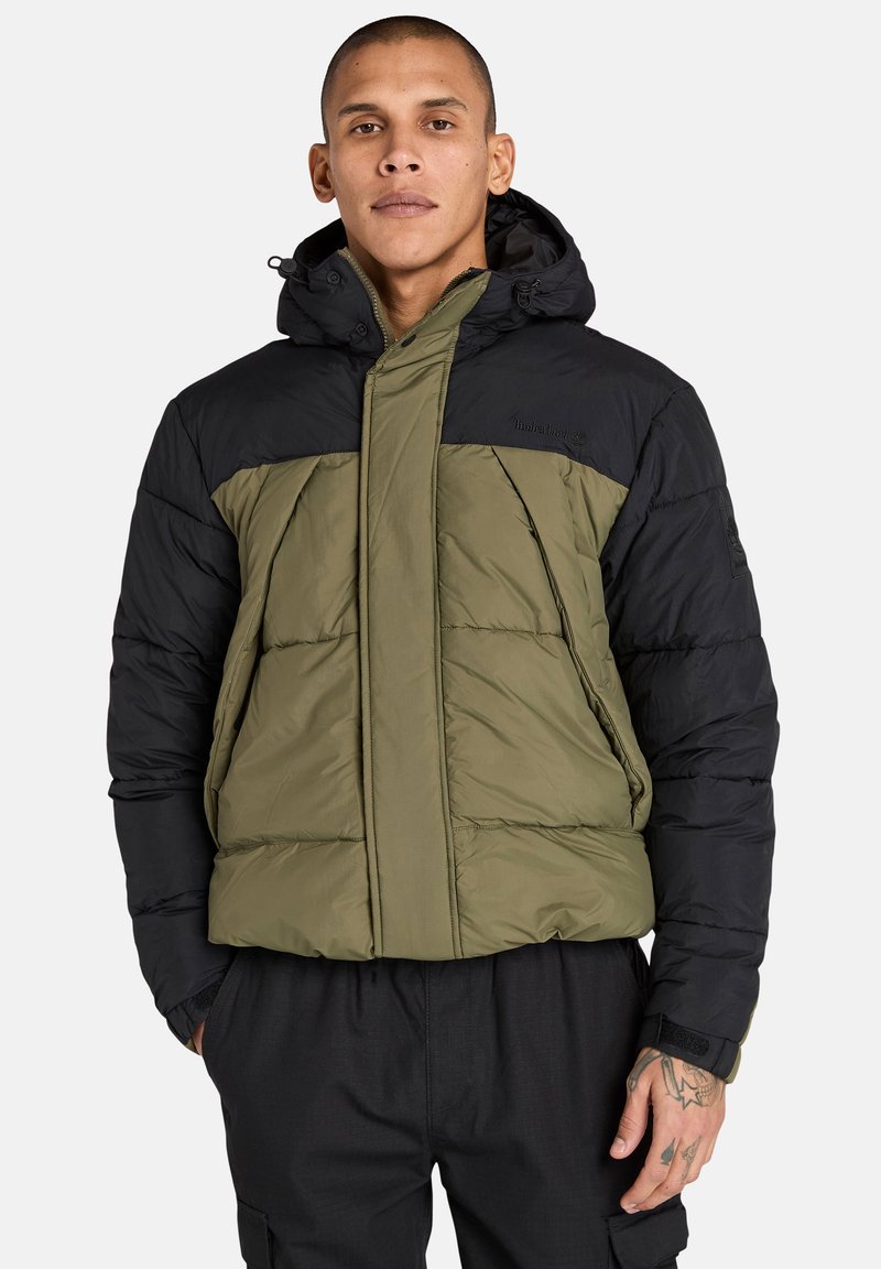 Puffjacka med en olivgrön och svart färgschema, med huva, dragkedja och quiltad textur. Försedd med en logotyp på axeln.