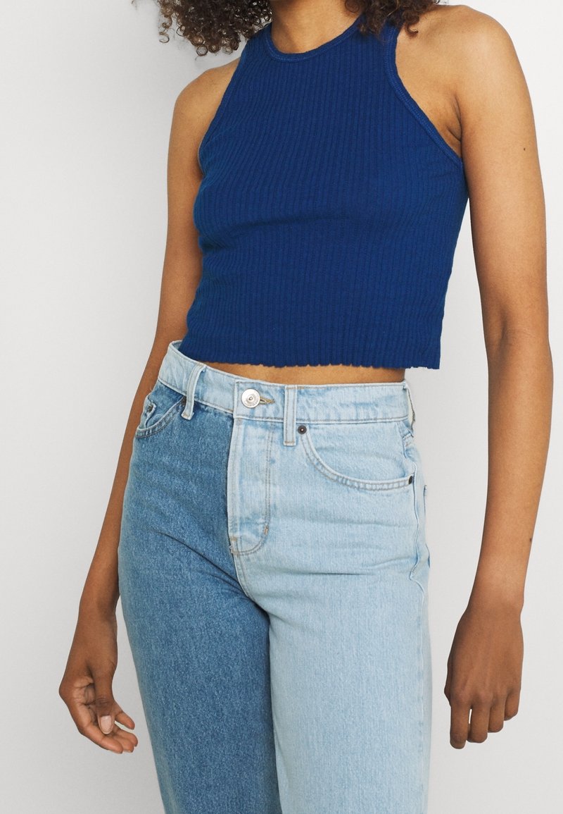 Pruhovaný modrý crop top s halter krkem, doplněný dvoubarevnými světle a tmavě modrými džínami s vysokým pasem a knoflíkovým zapínáním.