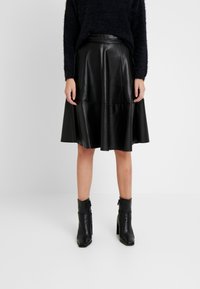 Svart läderkjol med en utsvängd design, med en mjuk textur och sömmar som detaljer. Matchad med svarta ankelstövlar.