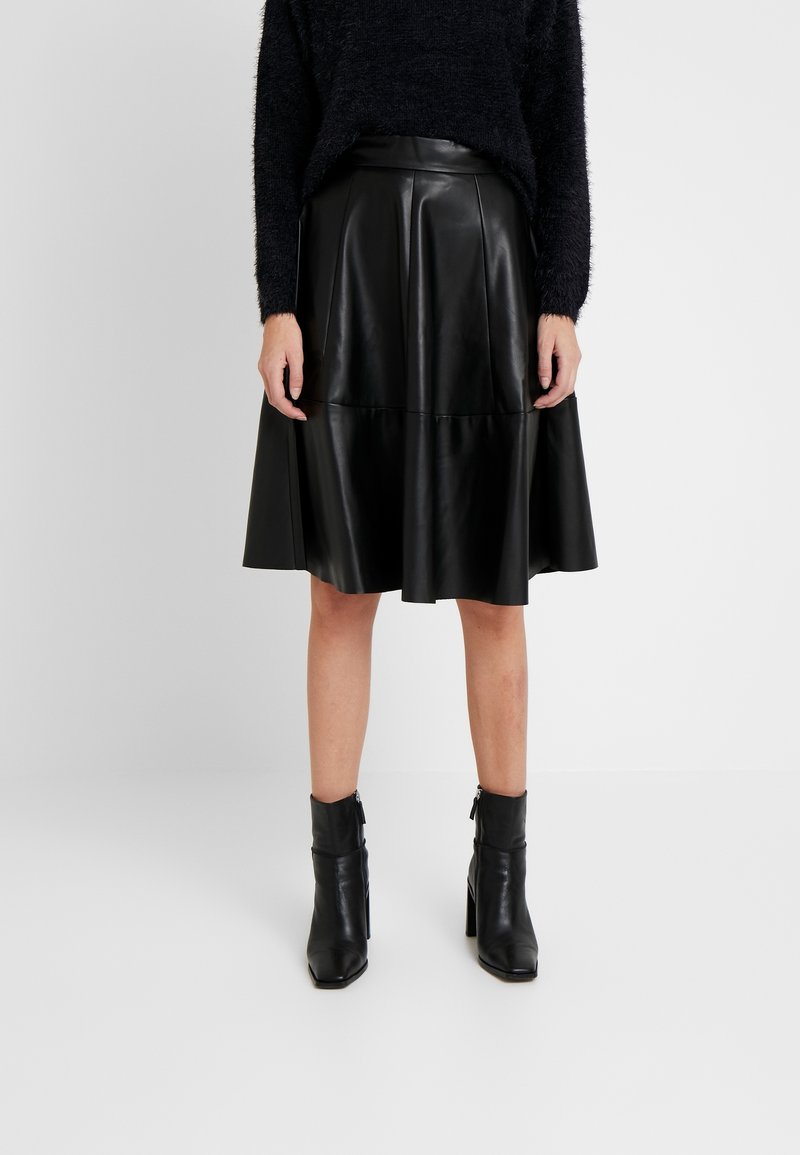 Svart läderkjol med en utsvängd design, med en mjuk textur och sömmar som detaljer. Matchad med svarta ankelstövlar.