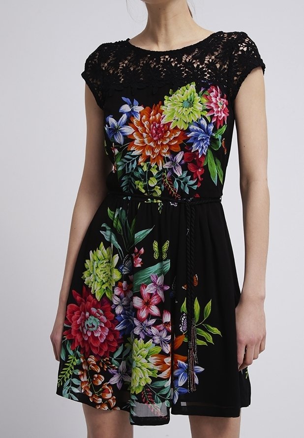 Schwarzes Kleid mit einem Spitzenansatz und bunten Blumenmustern mit Gänseblümchen, Sukkulenten und Schmetterlingen. Enthält einen Bindegürtel in der Taille.