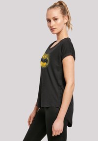 Svart kortermet t-skjorte med et gult og svart Batman-logo, med en avslappet passform og rund hals. Glatt stoffoverflate.