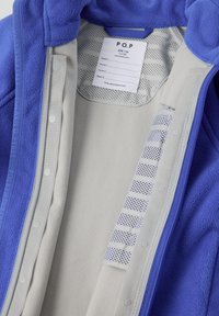 Fleecepaita sinisenä harmaalla vuorella. Varustettu neppari-napeilla sekä kauluksessa olevalla tarralla, jossa on hoito-ohjeet ja kokotiedot.