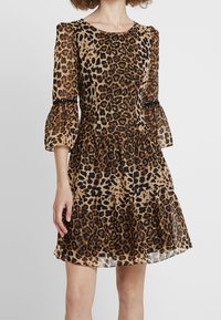 Robe à imprimé léopard avec un corsage ajusté, des manches évasées et une jupe à plusieurs couches. Fabriquée dans un tissu léger, elle présente des détails transparents et des accents noirs.
