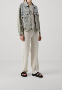 Světle modrá denimová bunda, bílé texturované pletené kalhoty a černé platformové sandály. Neformální outfit s uvolněným střihem a neutrální barevnou paletou.