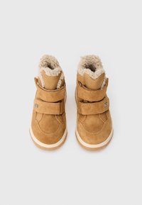 Braune Wildleder-Stiefeletten mit beigem Fleece-Futter, doppelten Klettverschlüssen und einer Gummisohle. Strukturiertes Stoffakzent am Knöchel.