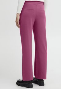 Wide-leg trousers in bright pink fabric with a smooth texture. Features two back pockets and a comfortable elastic waistband. Black platform shoes.