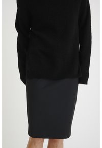 Svart tröja i mjukt, strukturerat material som bärs med en figurnära svart kjol. Båda plaggen har en sömlös design och en solid färg.