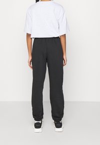 Grå oversized t-shirt med rund hals, svarta elastiska byxor med manschetter och svarta sportskor med vita sålar.