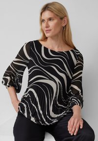 Schwarz-weiß gestreifte Bluse mit plissierter Textur, weitem Ausschnitt und schmalen Ärmeln, kombiniert mit dunklen Hosen.