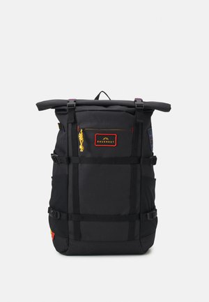 Mochila preta com fecho superior, alças ajustáveis, bolso frontal e bolsos laterais em rede. Apresenta um puxador amarelo e um patch de logotipo vermelho.