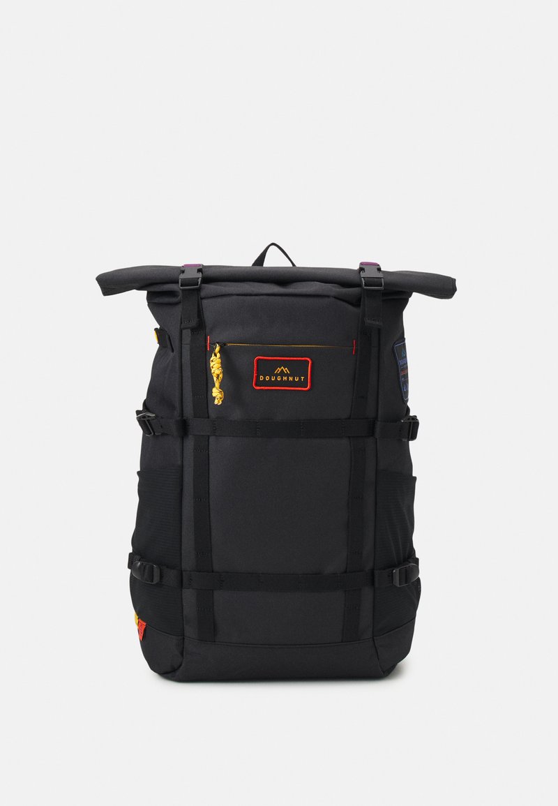 Rucsac negru cu rolă, cu curele ajustabile, buzunar frontal și buzunare laterale din plasă. Are o poartă de fermoar galbenă și un patch cu logo roșu.
