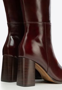 Paire de bottes mi-mollet en cuir marron foncé avec talons blocs superposés et détails de couture soignés sur fond blanc.