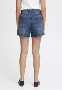 Shorts en denim avec un délavage bleu, taille haute, poches avant et coutures de poche arrière distinctes. Stylés avec des chaussures plates noires.
