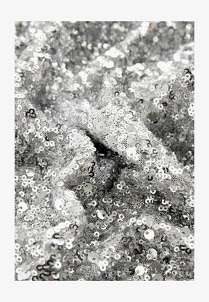 Tissu en sequins argentés avec un motif complexe de petits sequins circulaires, créant une surface réfléchissante et texturée qui semble froissée.