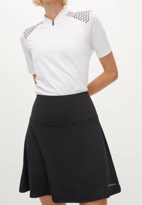 Vit, kortärmad topp med dragkedja och mönstrade axelaccenter, matchad med en svart, knälång kjol av slät, stretchig kvalitet.