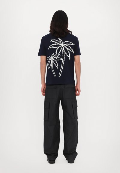 Marine T-shirt met een wit zigzag palmboom ontwerp op de achterkant. Gecombineerd met losse zwarte cargobroek met zijzakken.