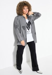 Camicia grigia a maniche lunghe con motivi a cuore sopra una maglietta bianca con la scritta "Love" in nero, abbinata a pantaloni neri e scarpe argentate.