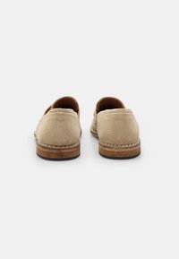 Bež semiš slip-on cipele s zaobljenim petama, šivenim detaljima i kontrastnom smeškom drvenom potplatom, s glatkom, teksturiranom površinom.