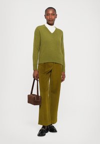 Olive green wool v-neck sweater paired with mustard corduroy wide-leg trousers. Model holds a small brown handbag and wears black shoes.