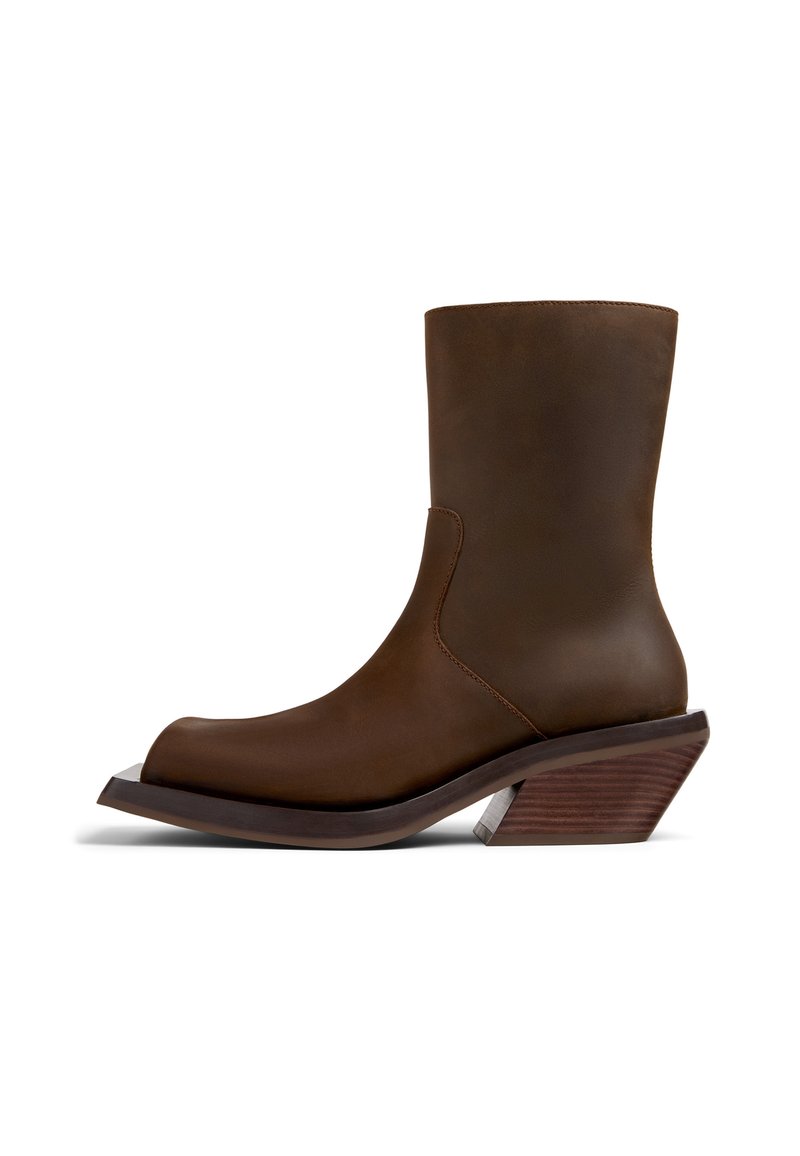 Bottine en cuir marron avec un bout pointu, texture lisse et un talon en bois angulaire distinctif. Détails de couture minimaux.