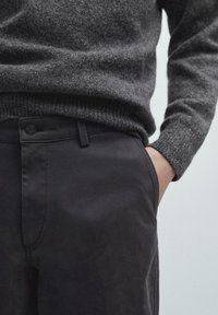 Szary wełniany sweter na ciemnoszarych dopasowanych spodniach, z zapięciem na guziki z przodu i boczną kieszenią, o gładkiej strukturze tkaniny.