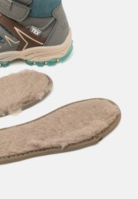 Botte de randonnée grise et teal avec une semelle intérieure brun texturé, présentant une surface pelucheuse, une semelle extérieure en caoutchouc et des sangles Velcro pour la fermeture.