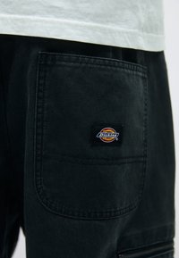 Crni platneni cargo šorts s velikom zakrpom, suptilnim šavovima i šarenom Dickies oznakom sa strane.