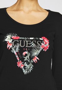 Maglietta nera a maniche lunghe con una grafica floreale e le scritte "GUESS" e "U.S.A." in decorazioni argentate, che mette in risalto un design a triangolo.