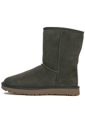 Donkergroene suède enkelboots met een ronde neus, verticale stiksels en een bruine rubberen zool. De schacht is lichtjes getextureerd.