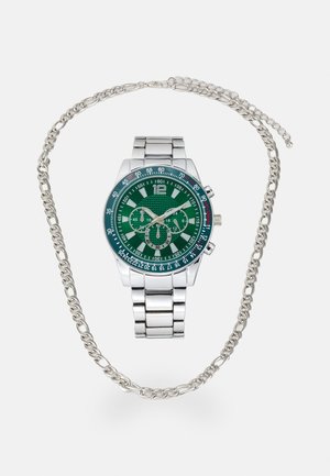 Montre en métal argenté avec un cadran texturé vert, présentant des index horaires blancs et des sous-dials ; accessoire en chaîne entrelacé avec la montre.