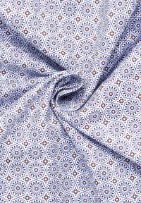 Tessuto leggero con uno sfondo bianco che presenta ripetuti motivi floreali in blu e marrone, che mostrano dettagli intricati e texture.