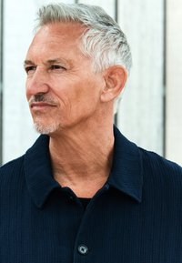 Marineblå tekstureret skjortejakke med krave og sort knaplukning, båret over en sort skjorte, med en naturlig baggrund.