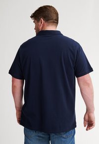 Marineblauw poloshirt met korte mouwen, een klassieke kraag, gladde stof en een relaxte pasvorm, gedragen met blauwe denim jeans.