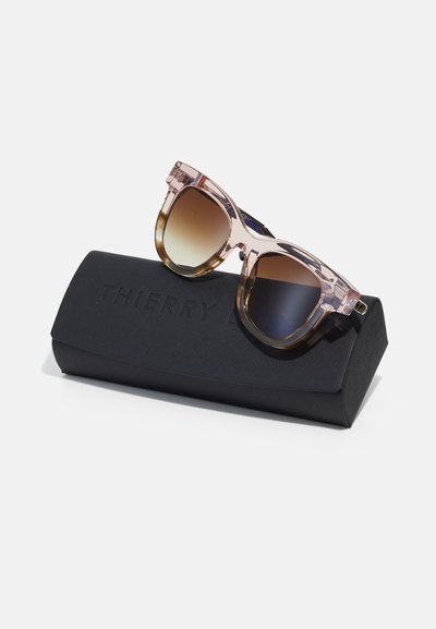 Lunettes de soleil à dégradé rose avec des accents marron dans un étui rigide noir portant le logo en relief "THIERRY". Monture en plastique lisse, forme arrondie.