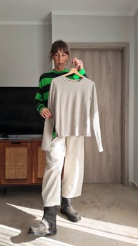 Svetlosivý top s dlhým rukávom a okrúhlym výstrihom, s bočnými rozparkami a voľným strihom, zavesený na drevenom vešiaku. Nosený pruhovaný zeleno-čierny sveter.