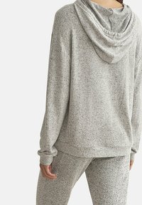 Sweat à capuche léger de couleur gris clair, texturé, avec une capuche et des manches longues. Il présente une coupe décontractée et des poignets côtelés. Tissu léger avec des éclats subtils.