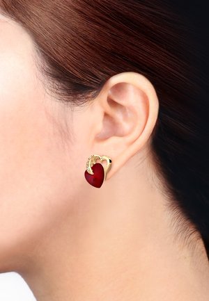 Ohrringe in Goldoptik mit einem roten herzförmigen Edelstein, akzentuiert mit einem kleinen glitzernden Detail und einem geschwungenen herzförmigen Design.