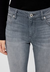 Vaqueros de mezclilla gris con un diseño ajustado, que cuentan con cierre de botón, estilo de cinco bolsillos y un sutil desgaste en la tela para dar textura.