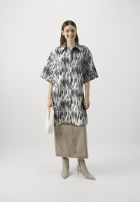 Svart og hvit mønstret skjorte med kort erme, kombinert med en beige denimskjørt og lysegrå spiss ankelstøvler. Hvit håndveske.