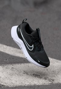 Sneaker atletico nero con tomaia in mesh, suola bianca e distintivo logo swoosh bianco. Presenta un colletto imbottito e un sistema di allacciatura.